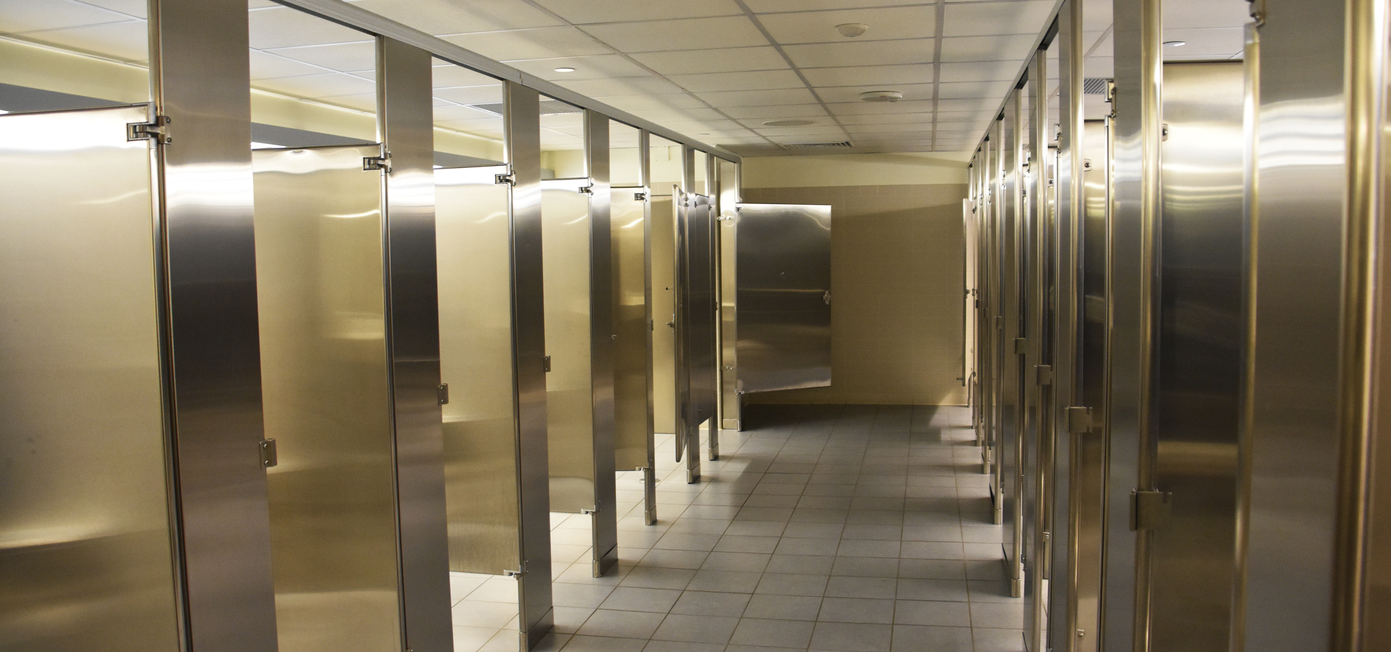 A perspective shot of a bathroom aisle banked on either side with 16 total stainless steel bathroom partitions, overhead brace, installed wall-to-wall style.